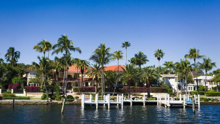 Scenic view of waterfront villas with palm trees and a pier under a clear blue sky.